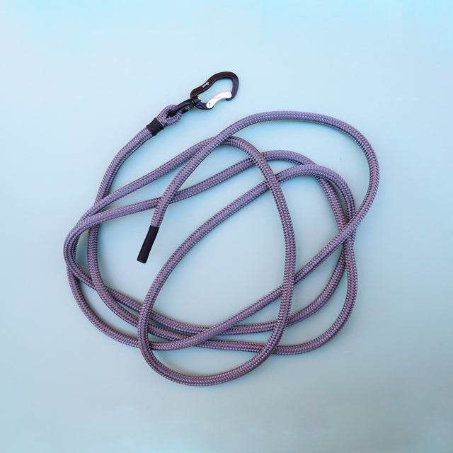A gray scent-work dog leash, with black metal carabiners and black waxed thread ends for grip, displayed on a blue background.