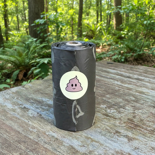Roll of dog waste bags with a smiley face sticker on a wooden surface outdoors