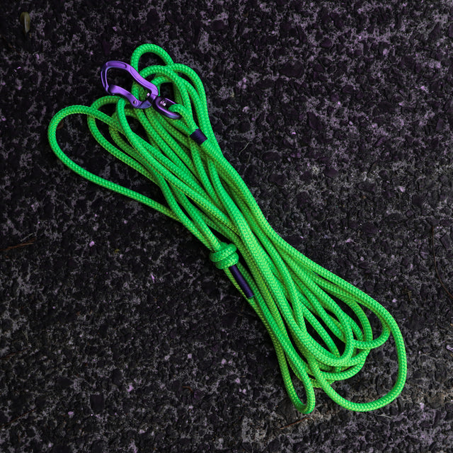 A fluro green dog long line with a purple carabiner and a knotted handle, laying on a textured surface.