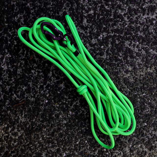 A fluro green dog long line with a knotted handle, laying on a textured surface.
